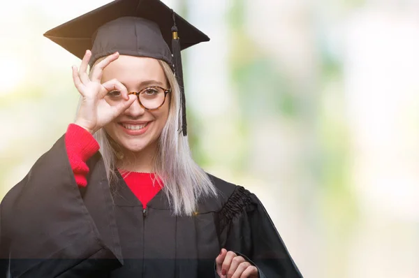 若いブロンドの女性の上の大学院の制服を着て笑顔 幸せそうな顔で指を通して見る目の手で のジェスチャーを行う背景を分離しました — ストック写真