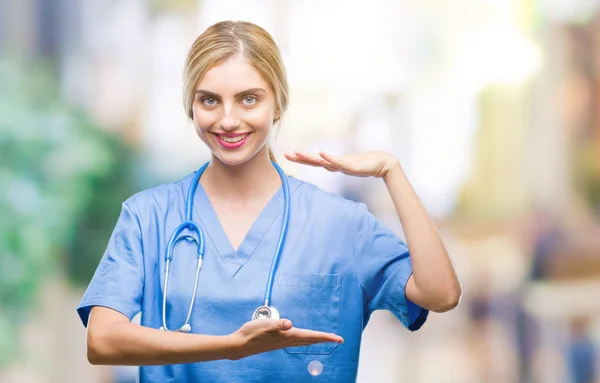 Young beautiful blonde doctor surgeon nurse woman over isolated background gesturing with hands showing big and large size sign, measure symbol. Smiling looking at the camera. Measuring concept.