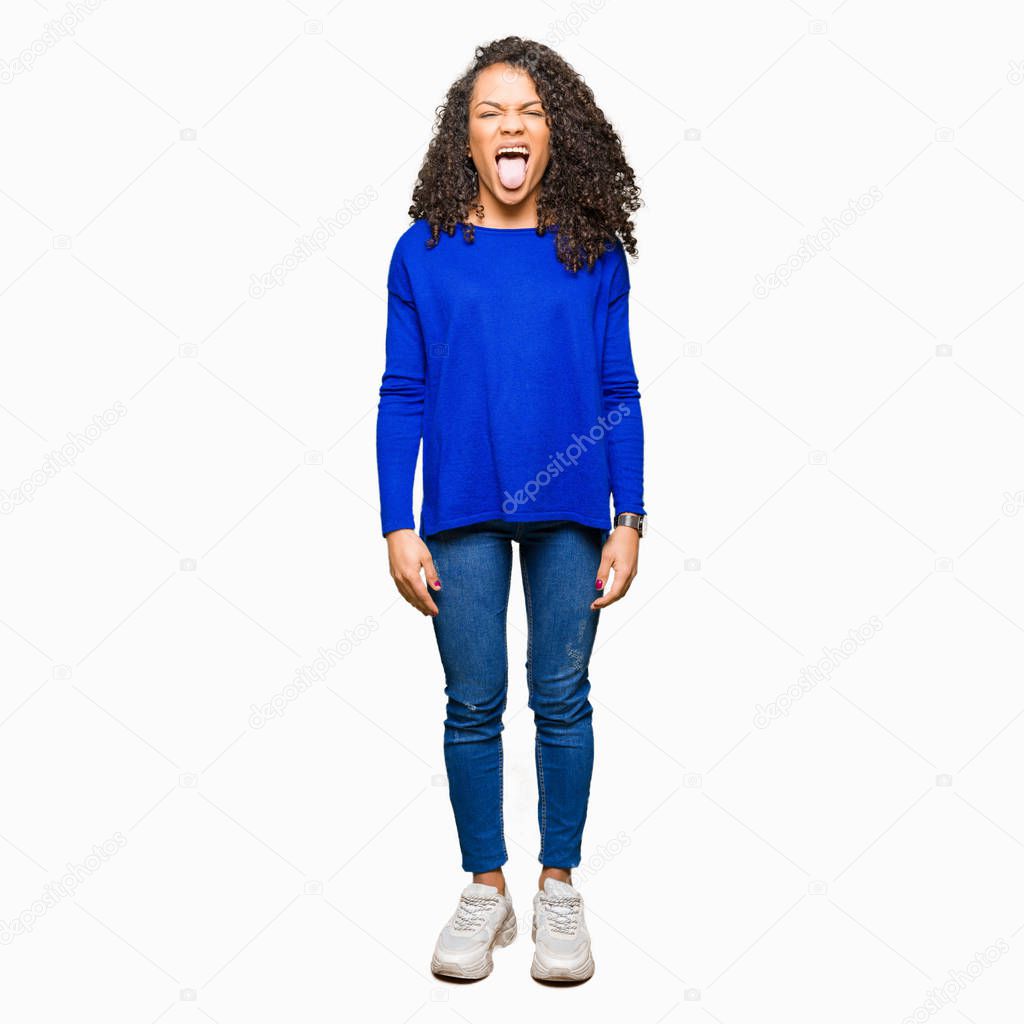 Young beautiful woman with curly hair wearing winter sweater sticking tongue out happy with funny expression. Emotion concept.