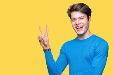 Genç yakışıklı adam mutlu yüz zafer işareti yaparken kameraya göz kırpıyor ile gülümseyen izole arka plan üzerinde mavi kazak giyiyor. İki numaralı.