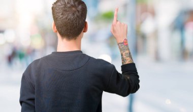 İzole genç yakışıklı adam arka plan geriye doğru arkasında parmak eliyle işaret Posing