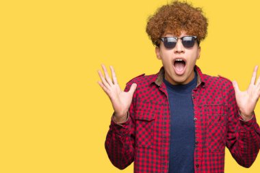 Yakışıklı genç afro saçlı deli kutluyor ve silah ile başarı için heyecanlı çığlık kaldırdı ve açık gözleri hayret güneş gözlüğü takıyor. Kazanan kavramı