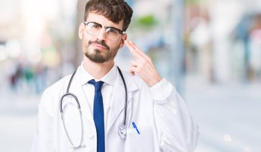 Genç doktor adam giyen hastane kat izole üzerinde çekim ve öldürmek kendini el ve parmaklara baş, intihar jest işaret arka plan.