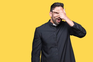 Genç Hıristiyan rahip yüz ve gözler el ile kapsayan şok bakmak izole arka plan üzerinde parmak utanç ifadesi ile üzerinden seyir.