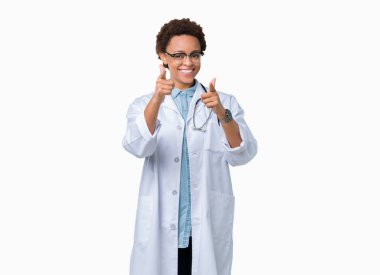 Genç Afro-Amerikan doktor kadın kamera ile mutlu ve komik yüz için parmakları işaret izole arka plan üzerinde tıbbi bir palto giyiyor. İyi enerji ve vibes.