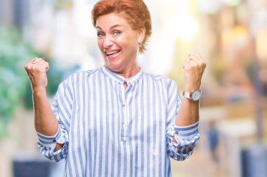 Atrractive üst düzey beyaz Kızıl saçlı kadın kutluyor izole arka plan üzerinde şaşırttı ve başarı için kaldırdı kollarını açarak hayret ve gözleri açık. Kazanan kavramı.