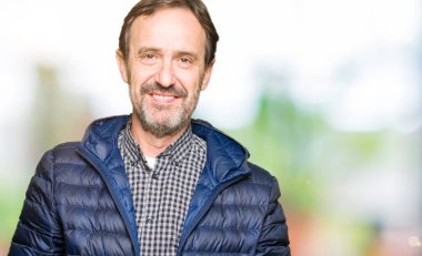 Orta yaş yakışıklı adam kış palto giyiyor birlikte elleri ve çapraz rahat ve neşeli gülümseyen parmak. Başarı ve iyimser