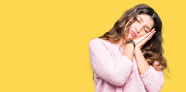 Rüya ve elleri ile kapalı gözler gülümseyen birlikte poz uyku pembe kazak giyen genç güzel kadın yorgun.