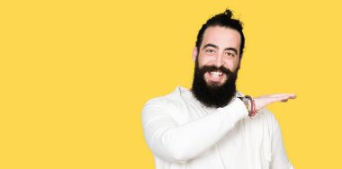 Uzun saç ve sakal sportif kazak eller eller büyük gösterilen ve büyük boy işareti, ölçü birimi sembolü ile giyen genç adam. Kameraya bakarak gülümsüyordu. Ölçüm kavramı.