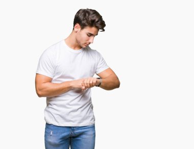 Kol saati, rahat ve kendinden emin zamanında kontrol izole arka plan üzerinde beyaz t-shirt giyen genç yakışıklı adam