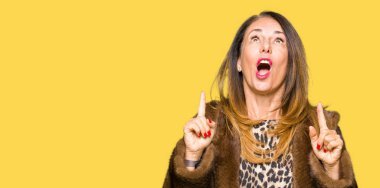 Güzel orta yaş zarif kadın giyiyor vizon hayret ve sürpriz ve parmakları ile işaret ceket ve silah kaldırdı.