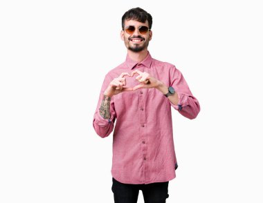 Genç yakışıklı adam aşık kalp simgesi ve elleriyle şekil gösteren gülümseyen izole arka plan üzerinde güneş gözlüğü takıyor. Romantik kavramı.