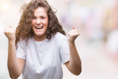 Güzel esmer kıvırcık saçlı Genç kız izole arka plan kutlama üzerinde rahat t-shirt giyen şaşırttı ve silah ile başarı için hayran kaldırdı ve gözleri açık. Kazanan kavramı.