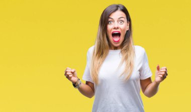 Genç güzel kadın kutluyor izole arka plan üzerinde rahat beyaz t-shirt şaşırttı ve silah ile başarı için hayran kaldırdı ve gözleri açık. Kazanan kavramı.