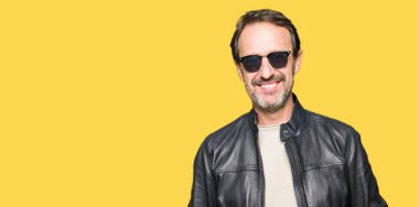 Orta yaş yakışıklı adam yüzünde güneş gözlüğü ve mutlu ve güzel bir gülümseme ile siyah deri ceket giyiyor. Şanslı kişi.