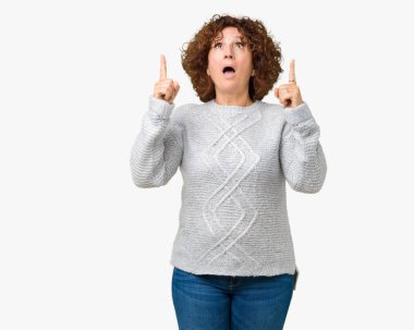 Hayret ve yukarıya bakıyor ve parmakları ile işaret ve silah kaldırdı sürpriz arka plan üzerinde kış kazak giyen güzel orta ager üst düzey kadın izole.