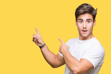 Gülümseyen ve iki elleri ve parmakları ile tarafına işaret kamera bakarak izole arka plan üzerinde beyaz t-shirt giyen genç yakışıklı adam.