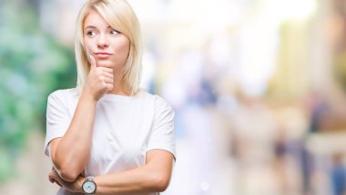 Çene düşünme hakkında soru, dalgın ifade üzerine el ile izole arka plan üzerinde beyaz t-shirt giyen genç güzel sarışın bir kadın. Düşünceli yüzüyle gülümsüyor. Şüphe kavramı.