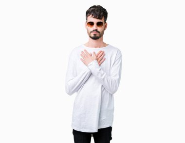 Yakışıklı delikanlı ile gülümseyen izole arka plan üzerinde güneş gözlüğü takıyor kapalı gözler ve yüzünde minnettar jest ile göğüs üzerinde eller. Sağlık kavramı.