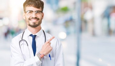 İzole arka neşeli bir gülümseme ile el ve parmak kadar yan yüzünde mutlu ve doğal ifade ile işaret yüz üzerinden hastane ceket giyen adam genç doktor