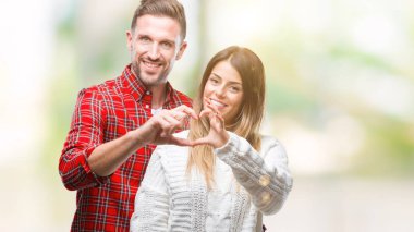 Genç çift aşık aşık kalp simgesi ve elleriyle şekil gösteren gülümseyen izole arka plan üzerinde kış kazak giyiyor. Romantik kavramı.