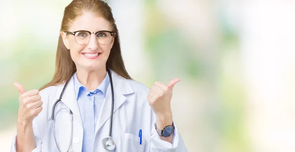 肯定的なジェスチャーを行う分離背景成功記号の上医療のコートを着て中年中高年医師女性の親指を笑顔と幸せ 勝者ジェスチャー晴れやかな表情でカメラを見てください — ストック写真