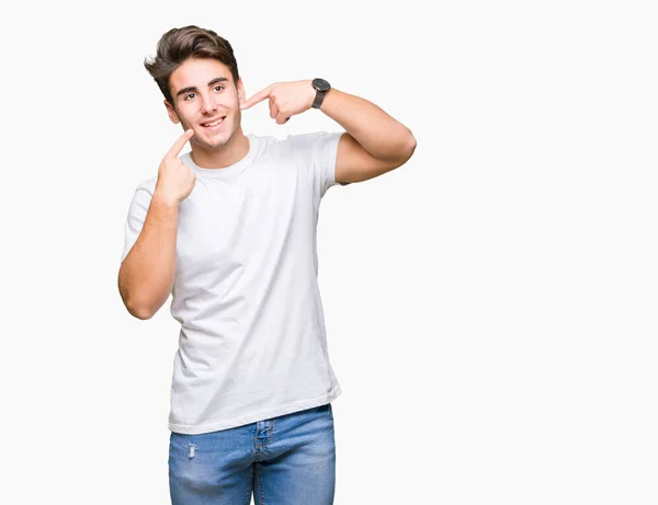 年轻英俊的男子穿着白色 T恤在孤立的背景下微笑着自信地显示和指着手指的牙齿和嘴巴 健康理念 — 图库照片