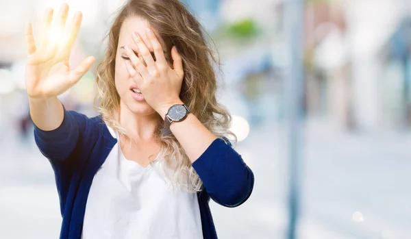 Beautiful young blonde woman over isolated background covering eyes with hands and doing stop gesture with sad and fear expression. Embarrassed and negative concept.