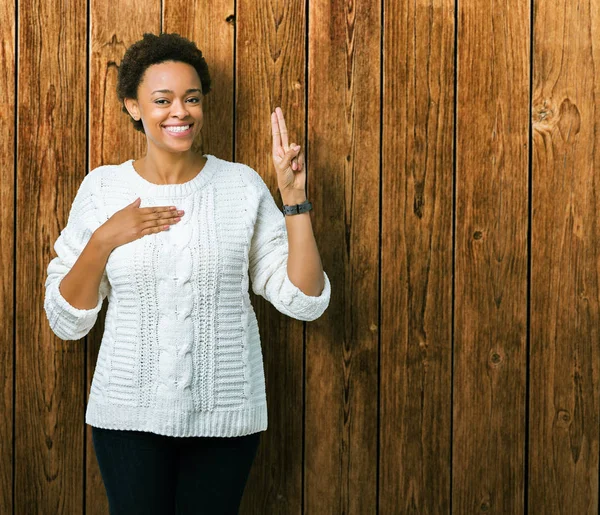 Beautiful young african american woman wearing sweater over isolated background Swearing with hand on chest and fingers, making a loyalty promise oath
