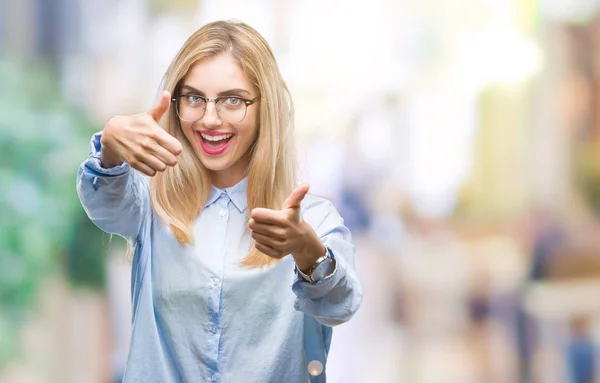 Young beautiful blonde business woman wearing glasses over isolated background approving doing positive gesture with hand, thumbs up smiling and happy for success. Looking at the camera, winner gesture.