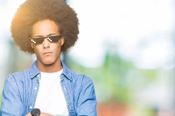 Young african american man with afro hair wearing thug life glasses skeptic and nervous, disapproving expression on face with crossed arms. Negative person.