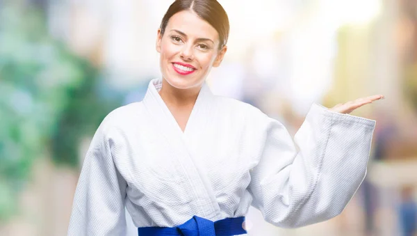 Young beautiful woman wearing karate kimono uniform over isolated background smiling cheerful presenting and pointing with palm of hand looking at the camera.