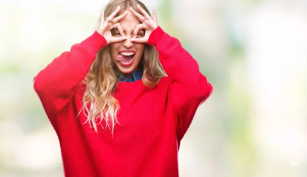 舌を出して指を通して見る目をこだわりの双眼鏡のような ジェスチャーを行う分離の背景に冬のセーターを着ている美しい若い金髪女性 クレイジー式 — ストック写真