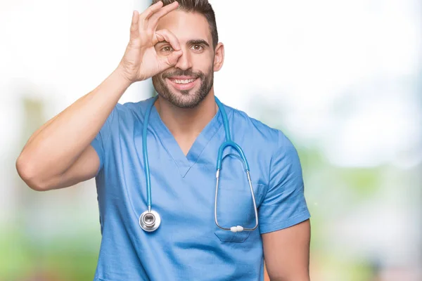英俊的年轻的医生外科医生在孤立的背景做确定的手势用手微笑 眼睛通过手指看与愉快的面孔 — 图库照片
