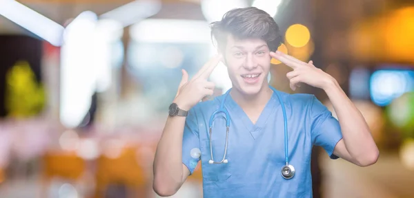 Joven Doctor Vistiendo Uniforme Médico Sobre Fondo Aislado Sonriendo Señalando —  Fotos de Stock