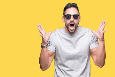 Yakışıklı delikanlı büyük gülümseme ile çığlık zaferini kutluyor ve ellerini kaldırdı izole arka plan çok mutlu ve heyecanlı, kazanan ifade üzerinde güneş gözlüğü takıyor