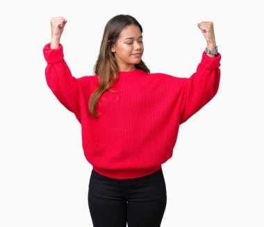 Kol kasları gururlu gülümseyen gösterilen izole arka plan üzerinde kırmızı kış kazak giyen genç güzel esmer kadın. Fitness kavramı.