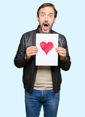 Kırmızı kalp şok sürpriz yüzü, korkuyor ve korku ifadesi ile heyecanlı olan korkmuş ile kağıt tutan yakışıklı orta yaş erkek