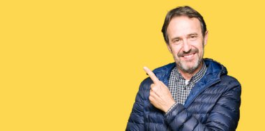 Orta yaş yakışıklı adam neşeli bir gülümseme ile el ve parmak kadar yan yüzünde mutlu ve doğal ifade ile işaret yüz ile bir kış palto giyiyor