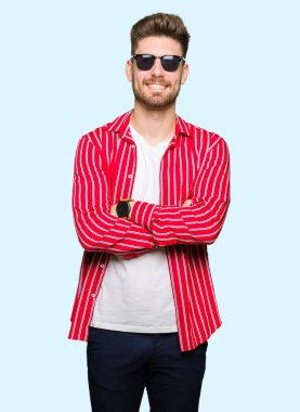 Genç yakışıklı gülen surat ile gülümseyerek kameraya seyir silah çapraz giyen güneş gözlüğü adam. Olumlu bir kişi.