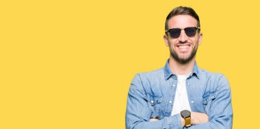 Moda güneş gözlüğü mutlu yüz çapraz silah kameraya bakarak ile gülümseyen giyen yakışıklı adam. Olumlu bir kişi.