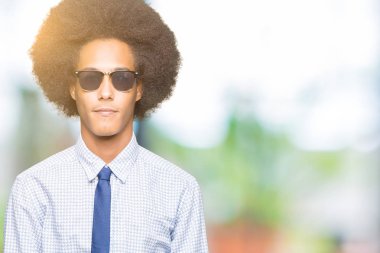 Yüzünde ciddi bir ifade ile güneş gözlüğü takıyor afro saçlı genç Afro-Amerikalı iş adamı. Basit ve doğal kameraya bakıyor.