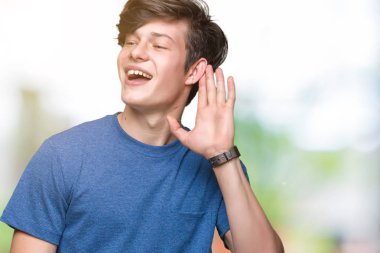 Bir işitme söylenti ya da dedikodu için dinleme kulak üzerinde el ile gülümseyen izole arka plan üzerinde mavi t-shirt giyen genç yakışıklı adam. Sağırlık kavramı.