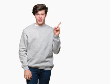Kameraya bakarak yan el ve parmak ile işaret yüzünde kocaman bir gülümseme ile izole arka plan üzerinde sweatshirt giyen genç yakışıklı sportif adam.