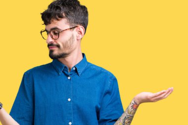 Gülen iki elle gösterilen açık avuç içi, sunma ve karşılaştırma ve denge reklam arka plan üzerinde gözlük takan genç yakışıklı adam izole