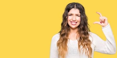 Beyaz kazak gülümseyen ve süre seyir ve kamera boyutu işaret parmaklarıyla yapıyor el ile kendine güvenen el hareketi giyen genç güzel kadın. Ölçü kavramı.