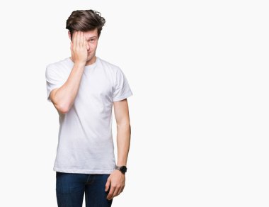 Üzerinde rahat beyaz t-shirt giyen genç yakışıklı adam arka plan kapsayan bir göz yüz ve sürpriz duygu kendinden emin gülümseme ile el ile izole.