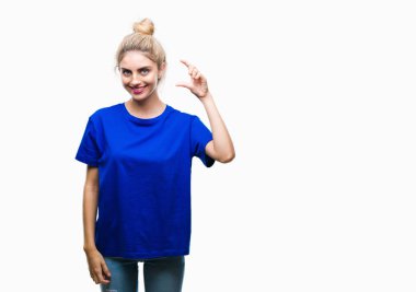 İzole arka plan gülümseyen ve boyutu işaret parmaklı ararken ve kamera işi el ile kendinden emin eller üzerinde mavi t-shirt giyen genç güzel sarışın ve mavi gözlü kadın. Ölçü kavramı.