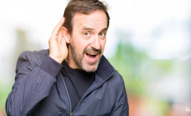 Orta yaş yakışıklı adam bir işitme söylenti ya da dedikodu için dinleme kulak üzerinde el ile gülümseyen bir ceket giyiyor. Sağırlık kavramı.