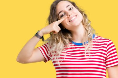 Güzel genç sarışın kadın yüzünden izole arka plan işaretçi el parmak yüz ve burun, neşeli gülümseyen